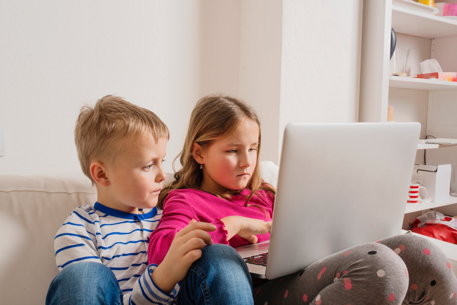 Children at home sitting on sofa, playing with laptop